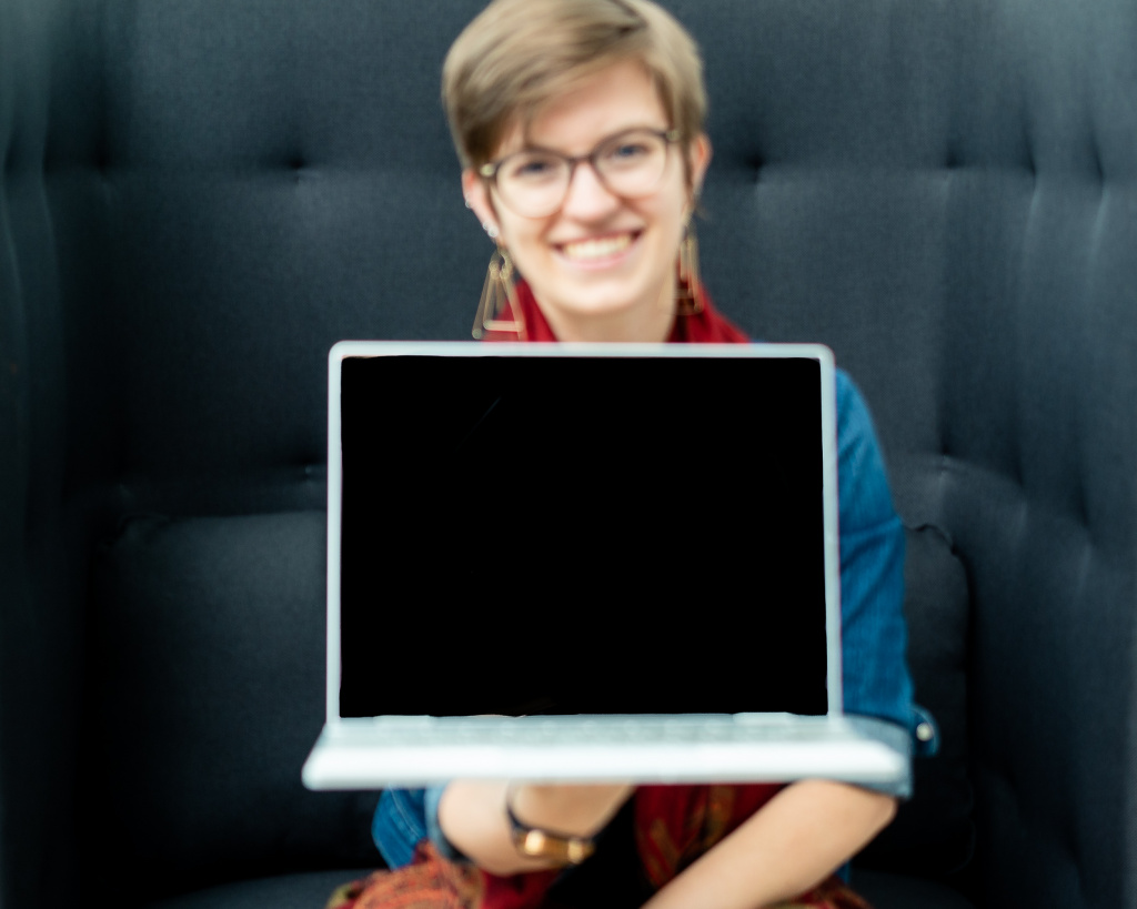 Female entrepreneur holds up laptop to show empty screen.